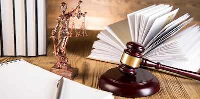 Legal symbols including Judge's gavel, Lady Justice statue, and law books on a wooden table.